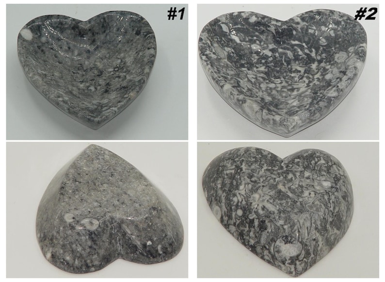 May include: Four heart-shaped decorative bowls. The bowls are made of gray stone with white veining. The bowls are in different orientations, showing the front, back, and side views. The bowls are on a white background.