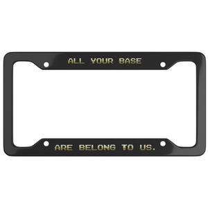 May include: Black license plate frame with the text "ALL YOUR BASE ARE BELONG TO US" in gold lettering. The frame has a rectangular shape with rounded corners and mounting holes.
