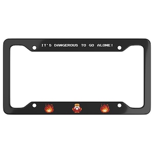 May include: Black license plate frame with the text "IT'S DANGEROUS TO GO ALONE!" and pixelated graphics of fire and a character. The frame is rectangular with rounded corners.