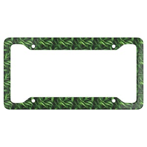 May include: Green leafy pattern license plate frame. The frame is made of metal and has a black background.