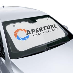 May include: White car windscreen sunshade with a black and white logo that says "Aperture Laboratories" and a stylised orange, blue and white circle logo.