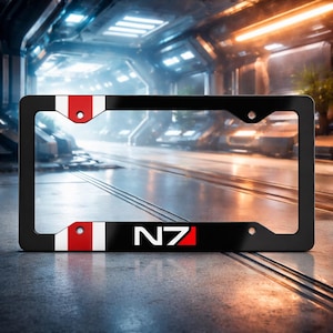 Puede incluir: Marco de matrícula negro con detalles en blanco y rojo. El marco muestra las letras "N7" en blanco con un acento rojo. Diseñado para una placa de matrícula estándar.