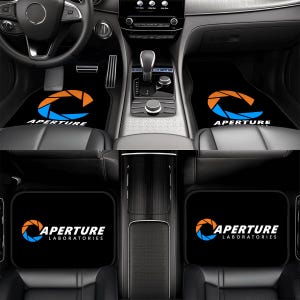 May include: Black car floor mats with the Aperture Laboratories logo in orange and blue. The logo is a stylized aperture shape with the word "Aperture" below it. The mats are designed to fit the front and back of a car.