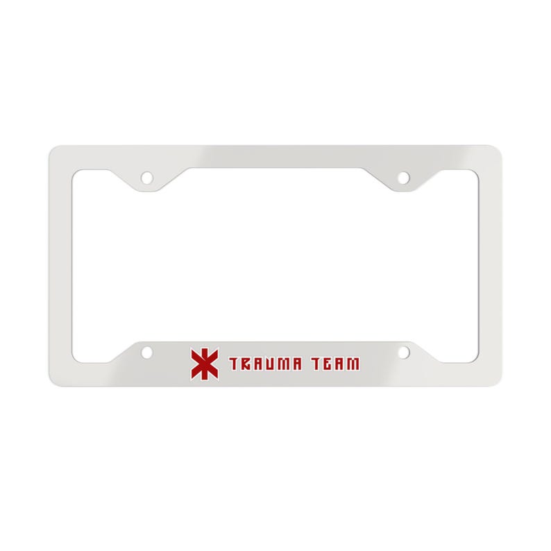 May include: A white rectangular license plate frame featuring a red six-pointed star of life symbol and the text TRAUMA TEAM printed in red block lettering on the bottom horizontal bar. The frame includes four circular mounting holes.