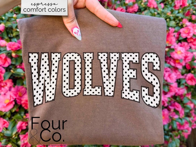 May include: A brown t-shirt with the word "WOLVES" in large, white, polka-dotted letters. The text "espresso comfort colors" is in the upper left corner. The brand name "Four & Co." is at the bottom.