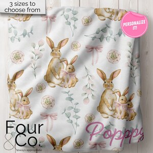 May include: A white baby blanket with a repeating pattern of brown bunnies, pink bows, green leaves, and pink flowers. The text "Four & Co. always appreciate" is at the bottom of the blanket. The text "Personalize it!" is in a pink circle at the top right corner of the blanket.