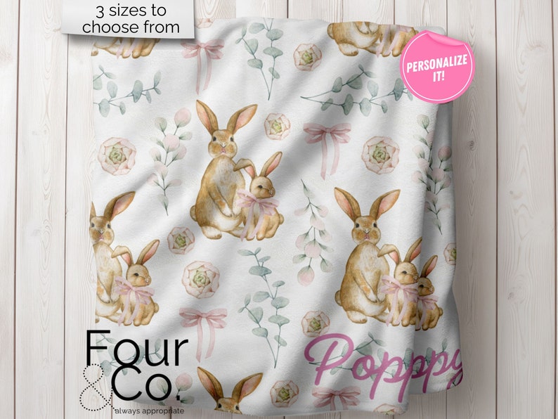 May include: A white baby blanket with a repeating pattern of brown bunnies, pink bows, green leaves, and pink flowers. The text "Four & Co. always appreciate" is at the bottom of the blanket. The text "Personalize it!" is in a pink circle at the top right corner of the blanket.