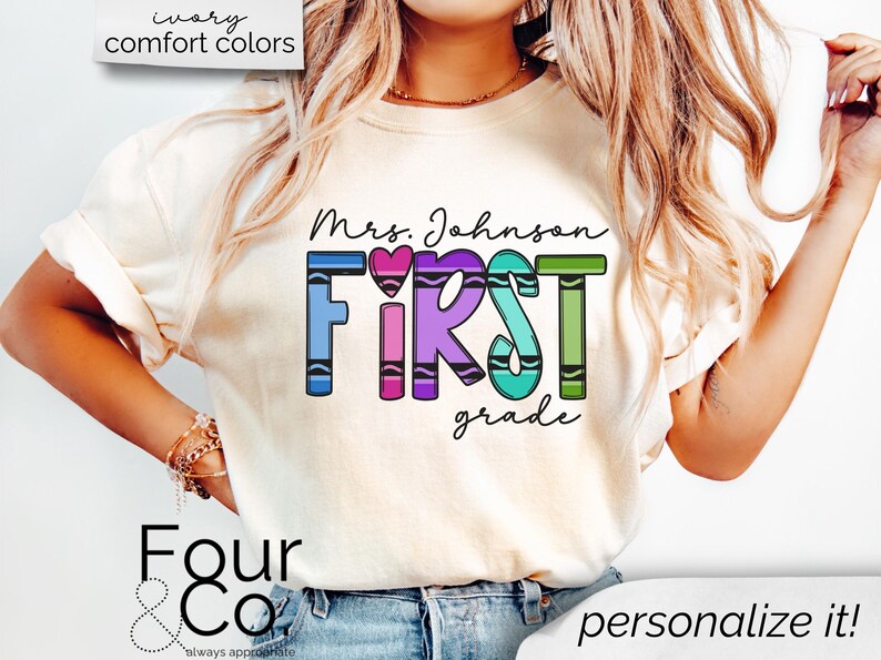 May include: A white t-shirt with the text "Mrs. Johnson FIRST grade" in rainbow colored crayon letters. The letters are outlined in black and have a small heart in the middle of the word "FIRST".