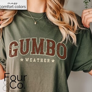 May include: A green t-shirt with the text "GUMBO WEATHER" in brown and white lettering. The shirt is a relaxed fit and has a distressed look. The text "Four & Co. always approachable" is printed in the bottom left corner.