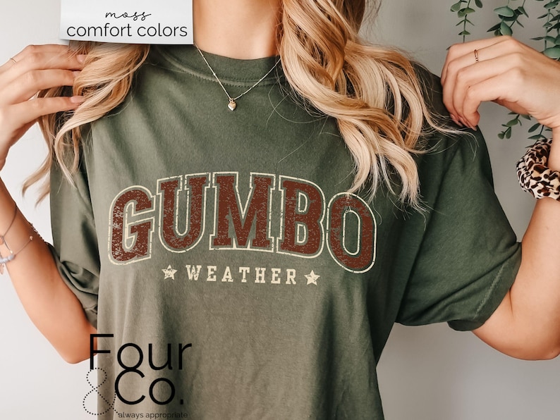 May include: A green t-shirt with the text "GUMBO WEATHER" in brown and white lettering. The shirt is a relaxed fit and has a distressed look. The text "Four & Co. always approachable" is printed in the bottom left corner.