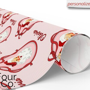 May include: A roll of pink wrapping paper featuring a repeating pattern of Santa Claus illustrations within oval frames, accented with red ribbons and the name "Olivia". The paper has a striped background and the text "Four Co." at the bottom.