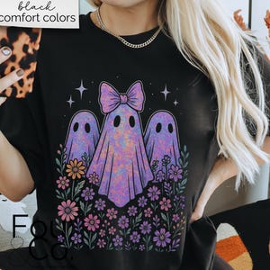 Puede incluir: Camiseta negra con un dise&ntilde;o de tres fantasmas morados con un lazo, rodeados de flores y estrellas. El texto "black comfort colors" est&aacute; en un cuadro blanco en la parte superior. Un dise&ntilde;o divertido y espeluznante.