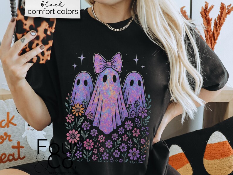 Puede incluir: Camiseta negra con un dise&ntilde;o de tres fantasmas morados con un lazo, rodeados de flores y estrellas. El texto "black comfort colors" est&aacute; en un cuadro blanco en la parte superior. Un dise&ntilde;o divertido y espeluznante.