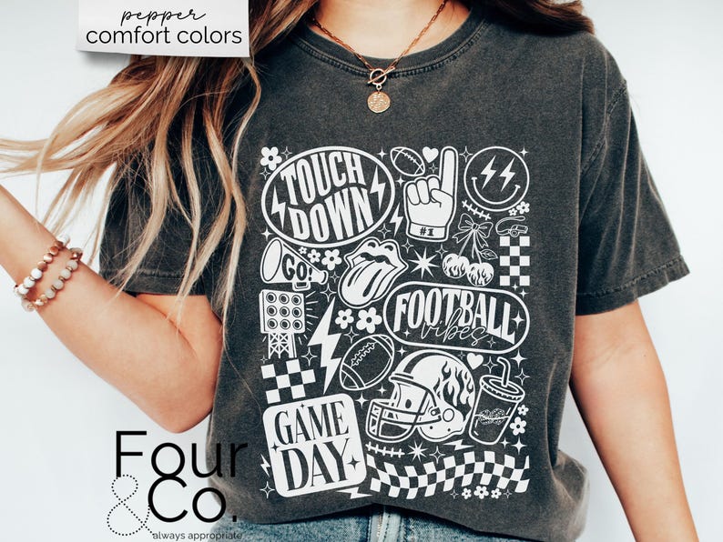 May include: Dark gray t-shirt with a white graphic design featuring football-themed elements like a helmet, football, and the words "Touchdown", "Football Vibes", and "Game Day". The shirt has the text "pepper comfort colors" at the top.