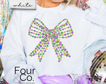 Puede incluir: Sudadera blanca con un diseño de lazo de cuentas de color morado, verde y dorado. El texto "Four & Co. always appropriate" está impreso en la parte inferior de la sudadera.