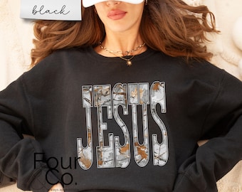 Puede incluir: Sudadera negra con la palabra "JESUS" en un diseño de camuflaje. La sudadera tiene cuello redondo y mangas largas. La palabra "black" está escrita en cursiva en la esquina superior izquierda.