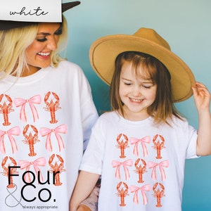 May include: Two white t-shirts with a pattern of pink bows and red lobsters. The text "Four & Co. always appropriate" is printed on the bottom of the larger shirt.