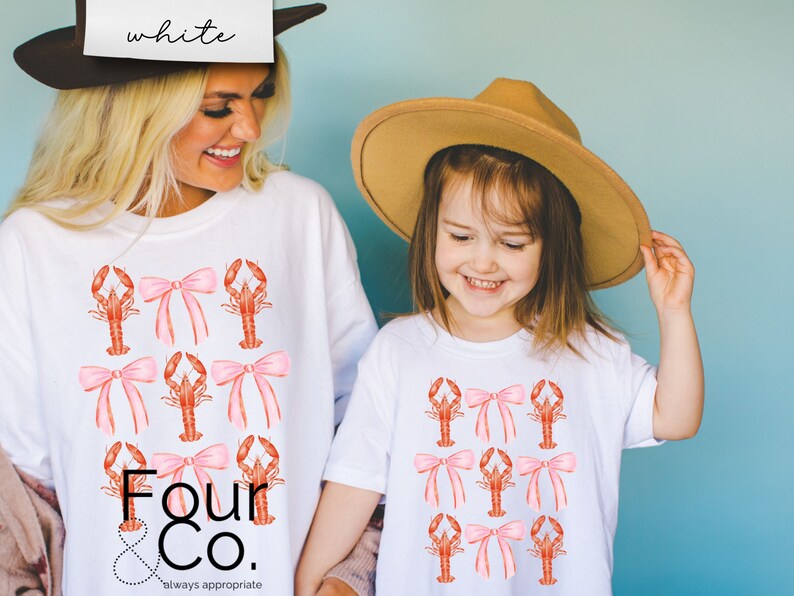 May include: Two white t-shirts with a pattern of pink bows and red lobsters. The text "Four & Co. always appropriate" is printed on the bottom of the larger shirt.