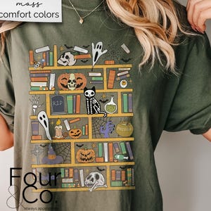 May include: A green t-shirt with a graphic of a bookshelf filled with spooky Halloween items, including a ghost, a pumpkin, a cat, and a potion bottle. The text "Four & Co. always appropriate" is printed on the bottom of the shirt.