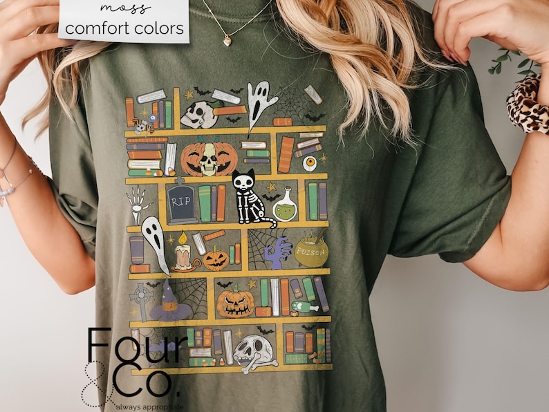May include: A green t-shirt with a graphic of a bookshelf filled with spooky Halloween items, including a ghost, a pumpkin, a cat, and a potion bottle. The text "Four & Co. always appropriate" is printed on the bottom of the shirt.