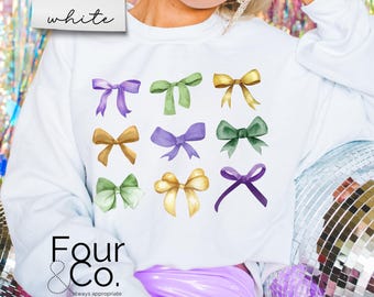 Puede incluir: Sudadera blanca con un gráfico de nueve lazos de acuarela en varios colores, incluyendo morado, verde y amarillo. El texto "Four & Co. always appropriate" está impreso debajo de los lazos.