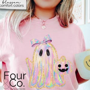 May include: Pink t-shirt with a holographic ghost wearing a bow and holding a pumpkin. The text "Four & Co. always appropriate" is on the bottom of the shirt.