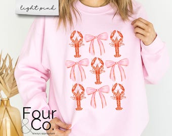Puede incluir: Sudadera rosa claro con un estampado repetido de langostas rojas y lazos rosas. La sudadera tiene mangas largas y cuello redondo. El texto "light pink" está en la esquina superior izquierda. El logotipo de la marca "Four & Co." está en la parte inferior.