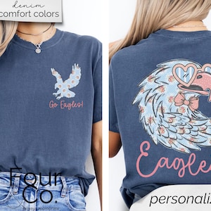 Pu&ograve; includere: T-shirt blu navy con un disegno di aquila sul davanti e sul retro. Il davanti presenta un'aquila floreale e la scritta "Go Eagles!". Il retro mostra un'aquila pi&ugrave; grande con occhiali a forma di cuore e la parola "Eagles".