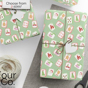 May include: Gift-wrapped presents with a festive green wrapping paper featuring playing card designs with Christmas themes. The gifts are tied with twine and a heart-shaped tag. A ball of twine and scissors are also visible.