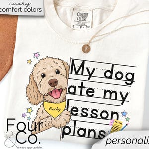 May include: A white t-shirt with a cartoon doodle of a dog with a yellow bandana that says "Rocky". The dog is peeking out from behind a sheet of lined paper with the text "My dog ate my lesson plans" written on it. The text "personalize it!" is written at the bottom of the shirt.
