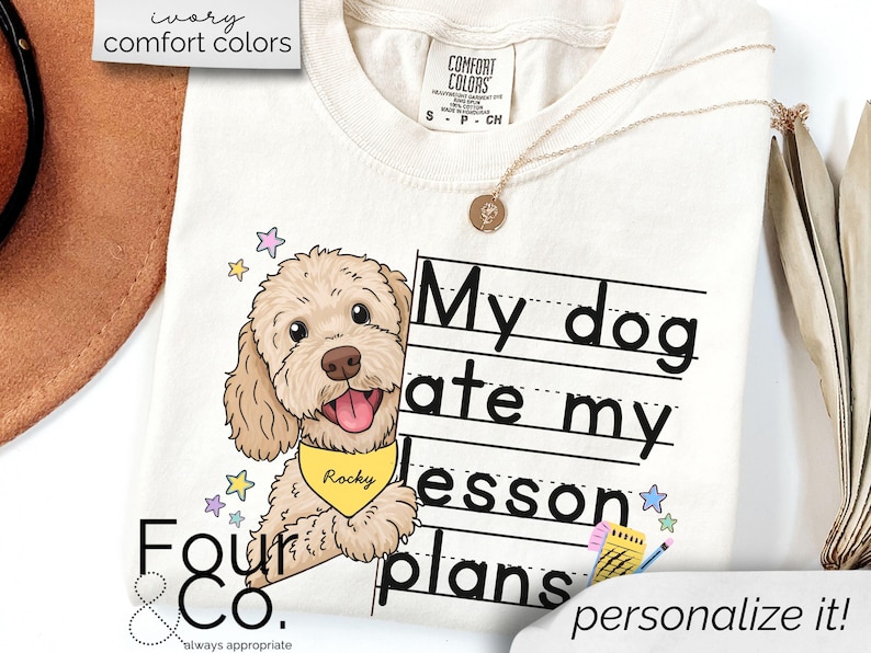 May include: A white t-shirt with a cartoon doodle of a dog with a yellow bandana that says "Rocky". The dog is peeking out from behind a sheet of lined paper with the text "My dog ate my lesson plans" written on it. The text "personalize it!" is written at the bottom of the shirt.
