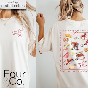 May include: A white t-shirt with the text "Crawfish Season" in red on the front and a graphic of crawfish and other food items in a red frame on the back. The shirt is from the brand "Four & Co."