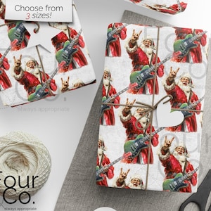 Könnte beinhalten: Geschenkpapier mit einem sich wiederholenden Muster von Santa Claus, der eine grüne E-Gitarre spielt und eine Rock'n'Roll-Handbewegung macht. Der Text "Choose from 3 sizes!" ist sichtbar. Eine Garnrolle und eine Schere sind ebenfalls vorhanden.