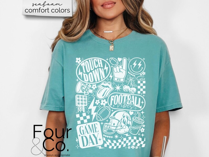 May include: A teal-colored t-shirt with a white graphic design featuring football-themed elements. The design includes the words "Touch Down", "Football Vibes", and "Game Day", along with footballs, a helmet, and other related icons. The shirt is part of the "comfort colors" collection.