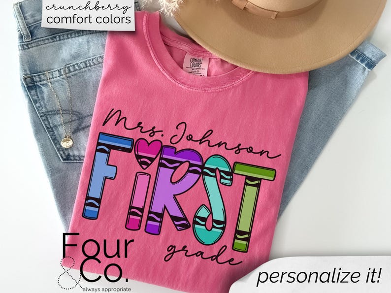 May include: Pink t-shirt with the text "Mrs. Johnson First Grade" in black lettering. The word "First" is made up of colorful crayon-shaped letters. The text "Four & Co. always appropriate" is at the bottom of the shirt.