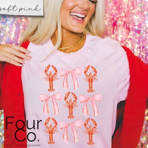 May include: A pink t-shirt with a graphic of red lobsters wearing pink bows. The text "Four & Co. always appropriate" is printed on the bottom of the shirt.