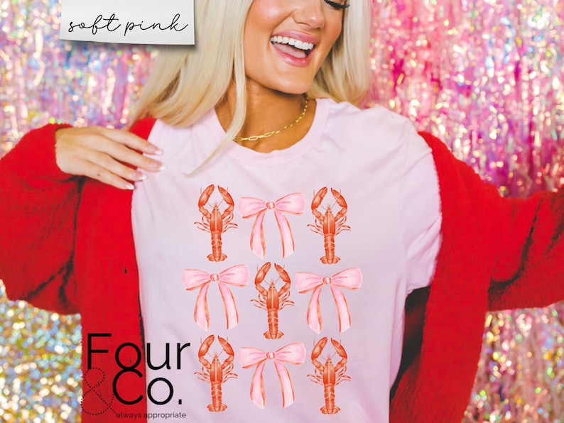 May include: A pink t-shirt with a graphic of red lobsters wearing pink bows. The text "Four & Co. always appropriate" is printed on the bottom of the shirt.