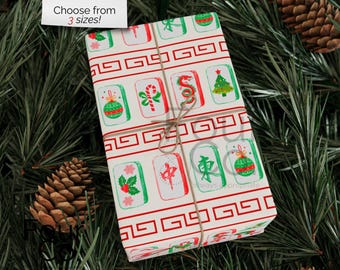 May include: Gift wrap with a festive design featuring red and green Mahjong tiles, candy canes, and Christmas trees. The wrapping paper is tied with twine and set against a backdrop of pine needles and pine cones. Text on the wrapping paper says "always appropriate".