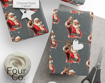 May include: Gift wrap featuring a repeating pattern of Santa Claus with a rock-and-roll hand gesture on a gray background. The wrapped gifts are tied with twine and have heart-shaped tags. A pair of scissors and a ball of twine are also visible.