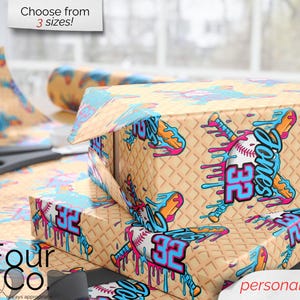 May include: Gift boxes and wrapping paper with a baseball theme. The design features a baseball bat, baseball, and the name "Jones" with the number "32" in blue and pink. The background is a waffle pattern. Text reads "Choose from 3 sizes!" and "personalize it!"