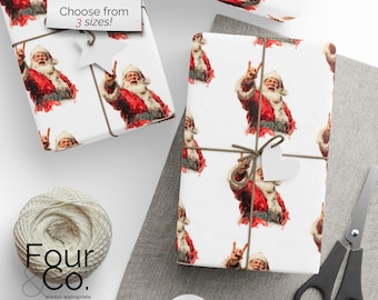 May include: White wrapping paper featuring a repeating pattern of Santa Claus giving the 'rock on' hand gesture. The wrapped gifts are tied with twine and have heart-shaped tags. A pair of scissors and a ball of twine are also visible.