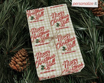 May include: A wrapped gift with a beige and white checkered pattern, tied with twine, and featuring the text "Merry Christmas Y'all" in red script. The gift is surrounded by pine needles and pine cones.