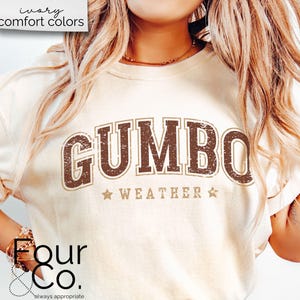 May include: A white t-shirt with a brown distressed graphic that says "GUMBO WEATHER" with two stars on either side of the text.