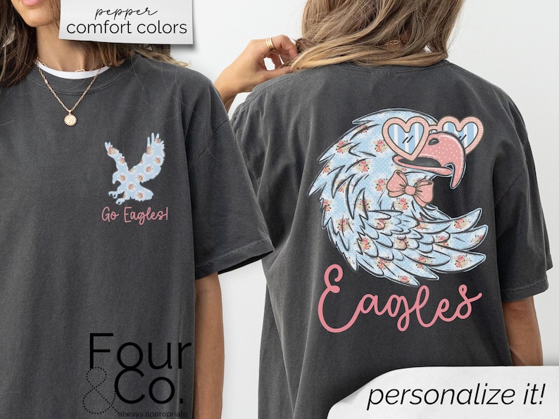 Pu&ograve; includere: T-shirt grigio scuro con un design floreale di aquila con occhiali da sole a forma di cuore e un fiocco. La parte anteriore ha una grafica di aquila pi&ugrave; piccola e le parole "Go Eagles!". La parte posteriore della maglietta ha la parola "Eagles" in corsivo.