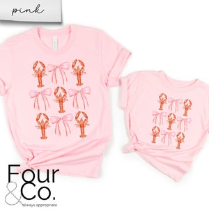 May include: Two pink t-shirts with a pattern of pink bows and orange lobsters. The larger shirt has the text "Four & Co. always appropriate" printed on the bottom.
