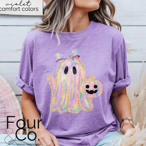 May include: A purple t-shirt with a holographic ghost holding a pumpkin. The ghost has a pink bow on its head. The text "violet comfort colors" is visible at the top of the image.