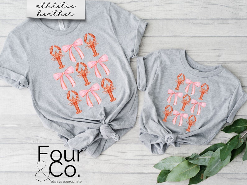 May include: Two grey t-shirts with a pattern of pink bows and orange lobsters. The larger shirt has the text "athletic heather" on the top and "Four & Co. always appropriate" on the bottom.