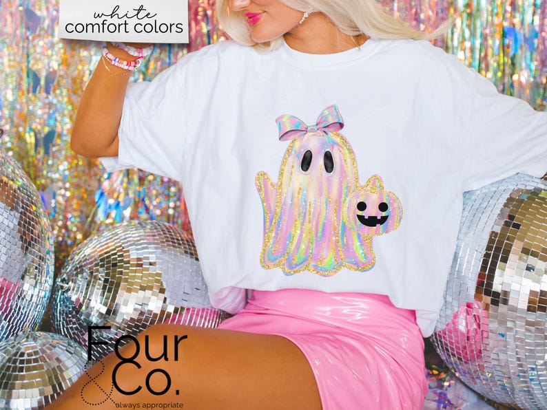 May include: White t-shirt with a holographic ghost holding a pumpkin. The ghost has a pink bow on its head. The text "Four & Co. always appropriate" is on the bottom of the shirt.