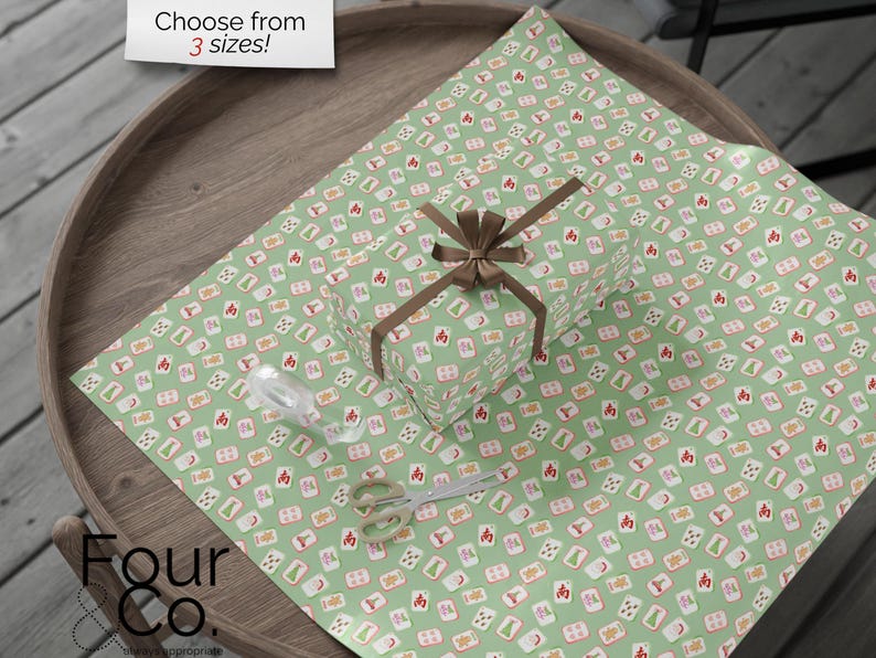May include: A wrapped gift with a brown bow sits on green wrapping paper patterned with red, white, and orange symbols. A pair of scissors and a roll of ribbon are also on the wrapping paper. The text "Choose from 3 sizes!" is in the top left corner.