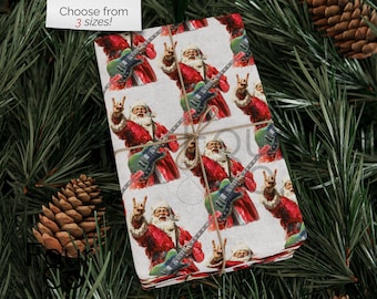 May include: Gift wrap featuring a repeating pattern of Santa Claus playing a green electric guitar and flashing a rock-and-roll hand gesture. The text "Choose from 3 sizes!" is in the upper left corner. The wrapped gift is tied with twine.